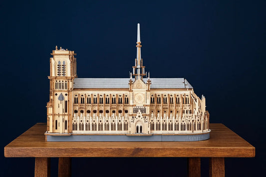 Maquette en bois détaillée de la cathédrale Notre-Dame de Paris, posée sur une table en bois devant un fond bleu uni.