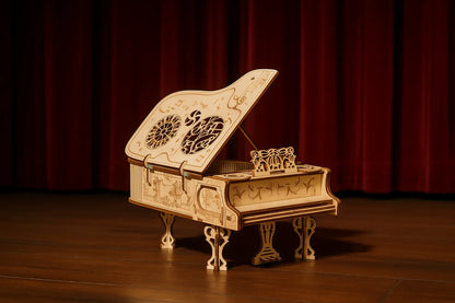 Maquette en bois de piano à queue ancien, délicatement gravée, posée sur une scène de théâtre avec rideau rouge en arrière-plan.