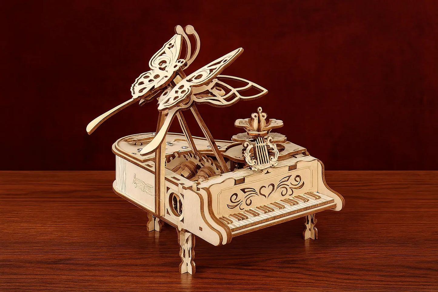 Maquette en bois d’un piano à queue miniature décoré de papillons finement découpés, présentée sur une table en bois devant un rideau rouge profond.