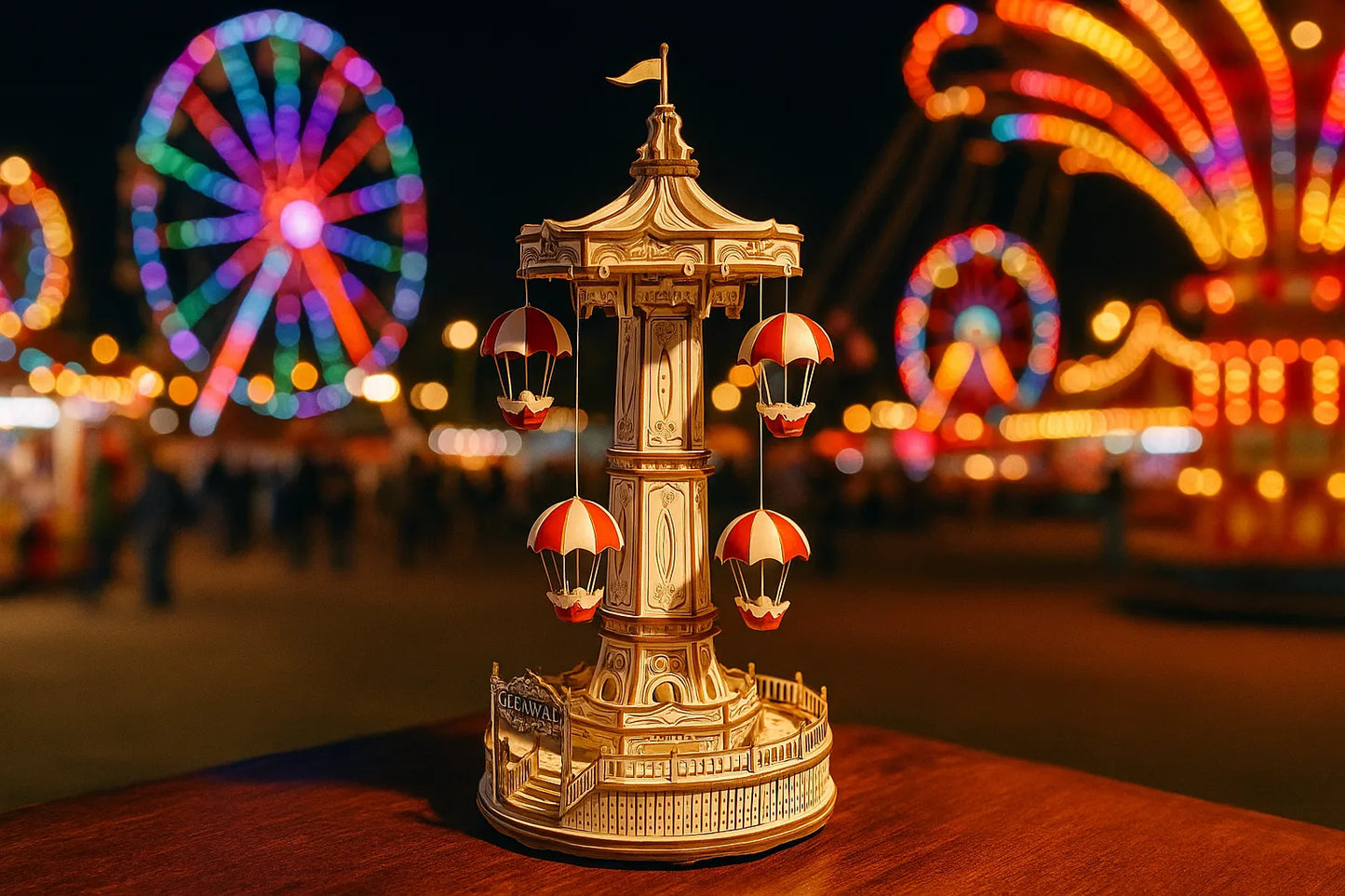 Maquette en bois d’une tour de parachutes avec nacelles rouges posée sur une table en bois devant une fête foraine éclairée.