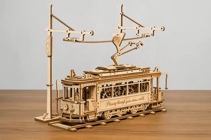Maquette en bois d’un tramway vintage avec caténaire posée sur une table en bois devant un mur gris clair.