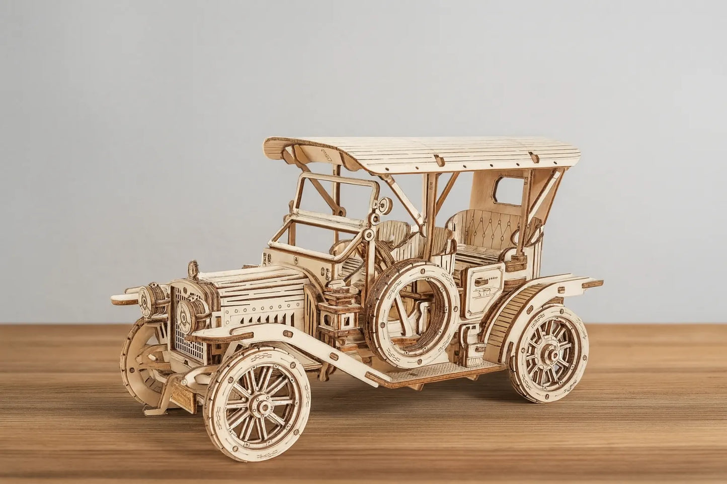 Maquette en bois d’une voiture ancienne de type Ford T posée sur une table en bois devant un mur gris clair.