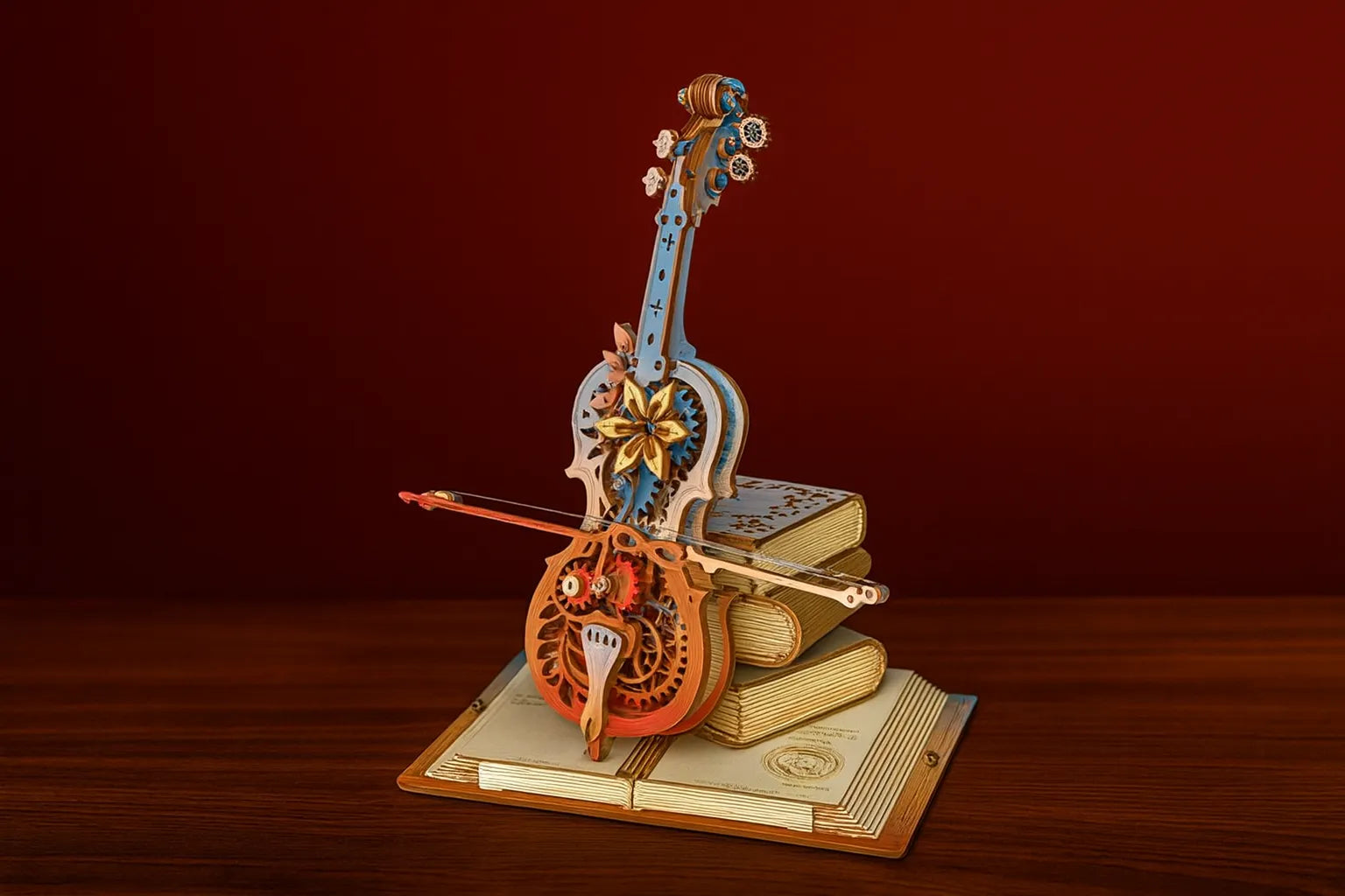 Maquette en bois colorée d’un violon fleuri, associant tons bleus et orangés, posée sur des livres ouverts sur une table en bois devant un fond rouge.