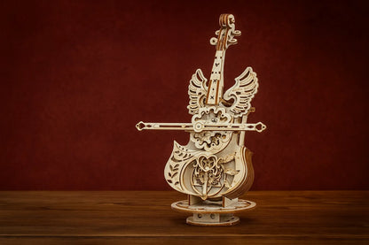 Maquette en bois d’un violoncelle élégant doté d’ailes d’ange sculptées, posée sur une table en bois devant un fond rouge texturé.