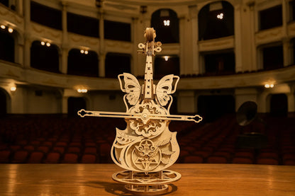 Maquette en bois d’un violoncelle mécanique orné d’ailes de papillons et de rouages apparents, exposée dans un théâtre classique à l’atmosphère feutrée.