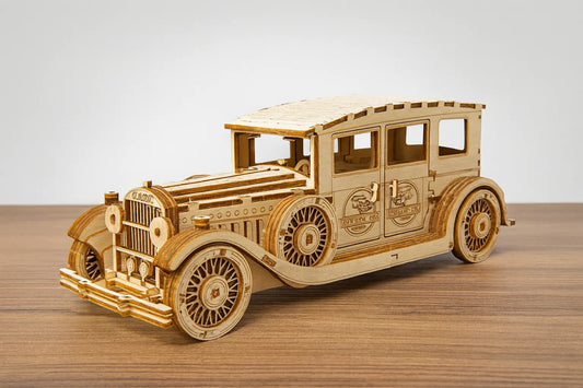 Maquette en bois d’une voiture classique à quatre portes avec l’inscription “Classic” sur la calandre, posée sur une table en bois devant un mur gris clair.