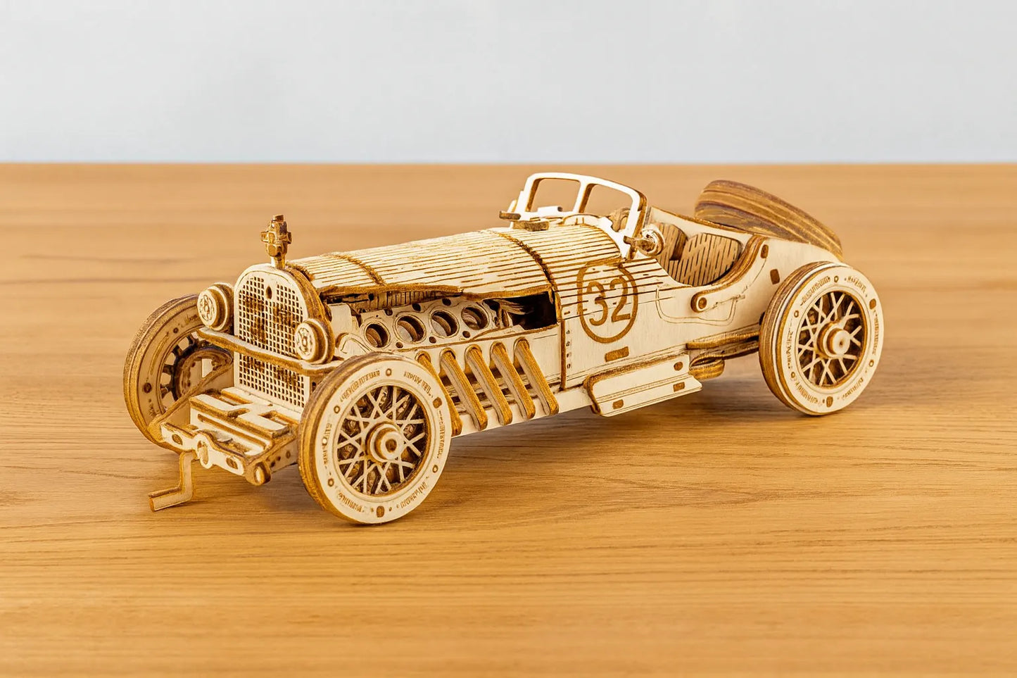 Maquette en bois d’une voiture de course vintage numéro 32, au style rétro, placée sur une table en bois devant un mur gris clair.