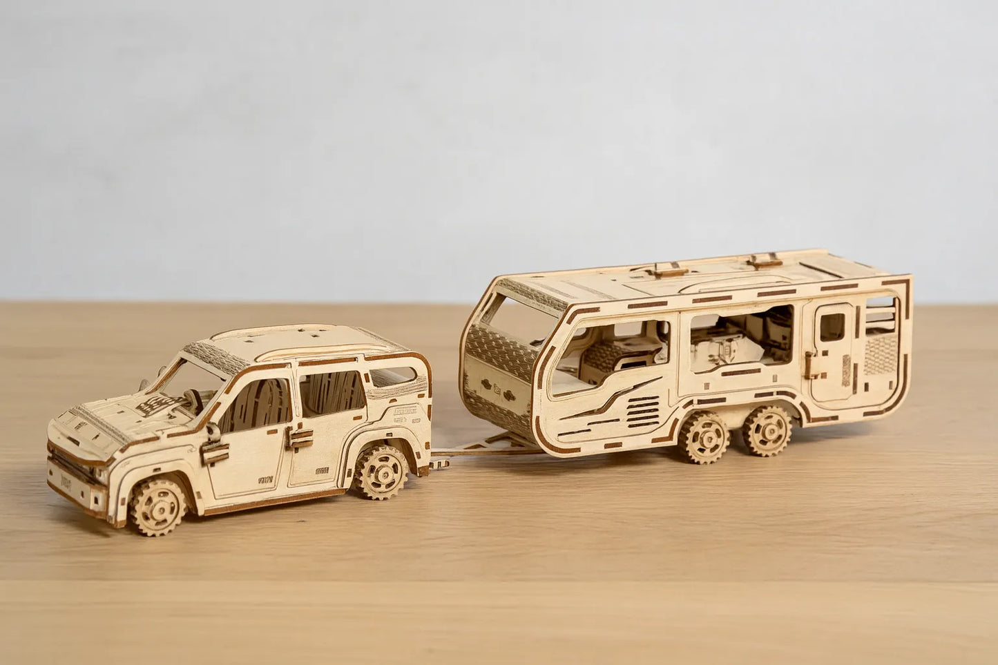 Maquette en bois d’un véhicule tout-terrain tirant une caravane, posée sur une table en bois devant un mur gris clair.