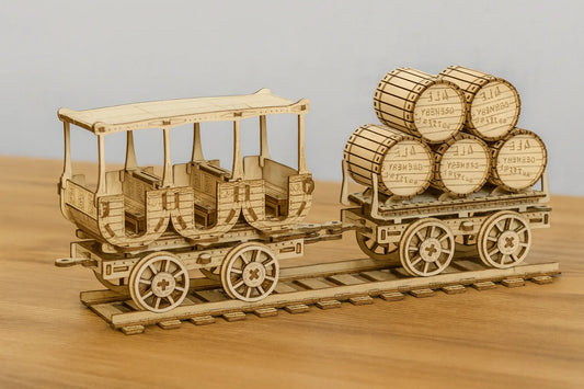 Maquette en bois d’un wagon de train ancien avec banquettes ouvertes, suivie d’un chariot transportant des tonneaux, posée sur une table en bois devant un mur gris clair.